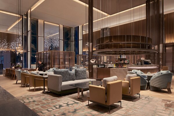 Un vestíbulo moderno de hotel con una zona de estar, un bar y una columna decorativa grande.