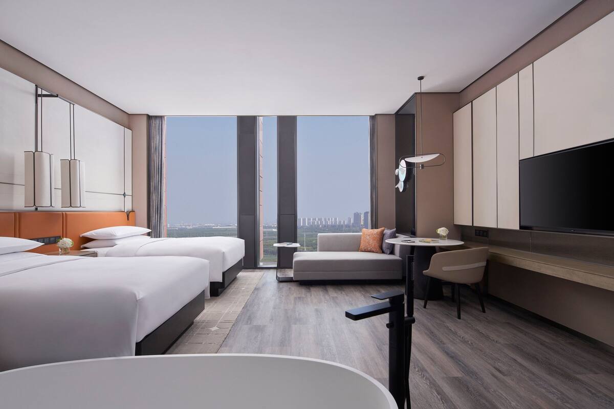 Una habitación de hotel moderna con dos camas, un sofá, un comedor y un televisor grande.