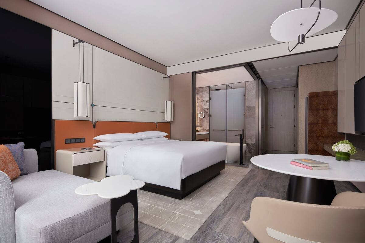 Una habitación de hotel moderna con una cama grande, un sofá, una mesa redonda y un escritorio pequeño.