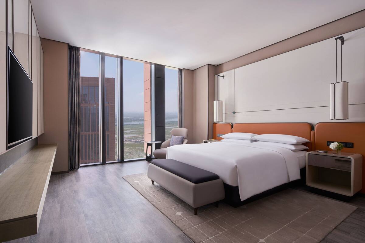 Habitación de hotel moderna con una cama grande, zona de estar, televisor y vista a la ciudad.