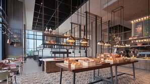 A modern restaurant with a long communal table, hanging pendant lights, and a variety of food displays. - Four Points By Sheraton Tianjin National Convention And Exhibition Center (Tianjin)