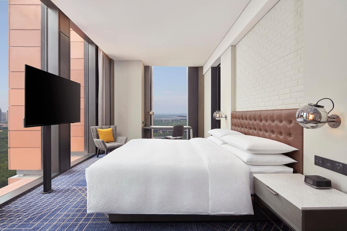 Ein Hotelzimmer mit einem großen Bett, einem Flachbildfernseher, einem Schreibtisch und Blick auf die Stadt.
