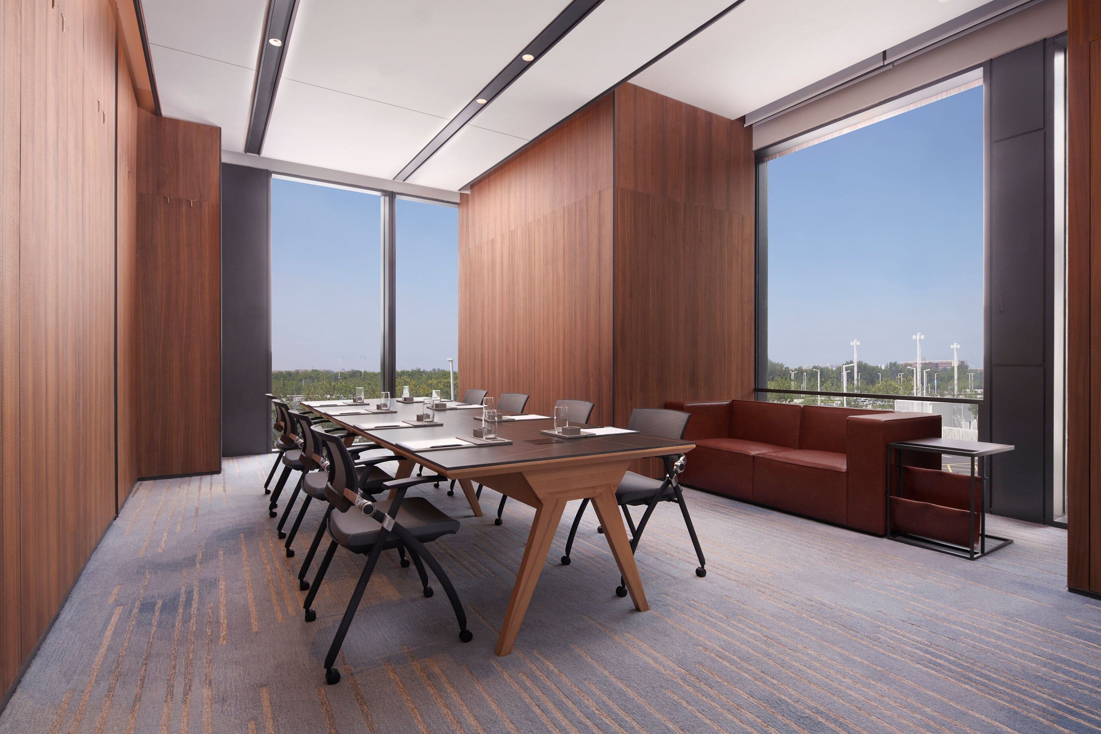 A modern conference room with a large table, chairs, a sofa, and large windows offering a city view.