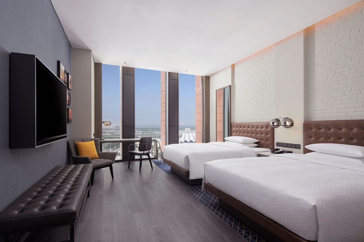 Ein Hotelzimmer mit zwei Betten, einer Bank, einem Schreibtisch und einem Fernseher.