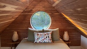 A cozy attic bedroom with a wooden sloped ceiling, a round window, and two woven baskets on nightstands.