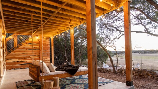 A wooden deck with a hanging swing, a patterned rug, and a view of the surrounding landscape.