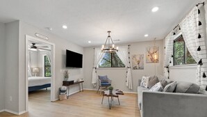 A modern living room with a grey sofa, a TV, a chandelier, and artwork on the walls.