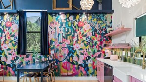 A vibrant kitchen with a colorful floral mural, wooden dining table, and pink cabinets. - Treetop House: King Loft & Outdoor Soaking Tub | Wimberley Hill Country (Wimberley)
