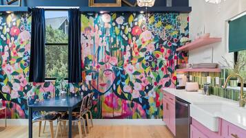 Une cuisine chaleureuse, agrémentée d’une fresque murale aux motifs floraux colorés, d’une table à manger en bois et de placards roses.