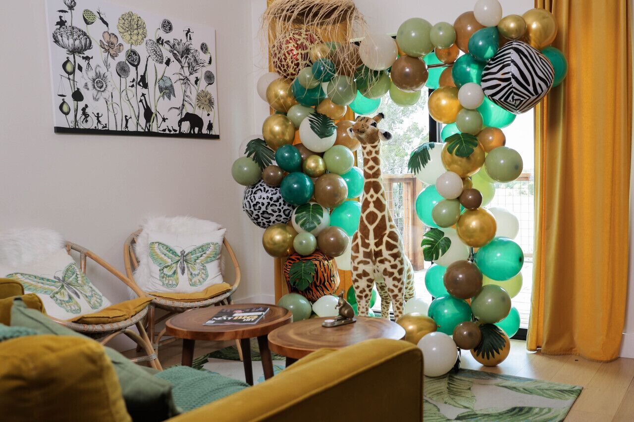 Une pièce décorée d’une statue de girafe, de ballons verts et dorés, et d’un tableau représentant des animaux.