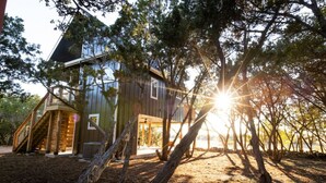 Un chalet rustique avec un escalier en bois, entouré d’arbres et sous un ciel dégagé.