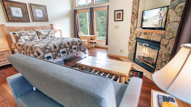 A cozy bedroom with a bed, a grey sofa, a fireplace, and framed pictures on the wall.