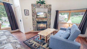 A cozy living room with a stone fireplace, a blue sofa, a wooden coffee table, and a patterned rug.