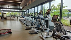 Une salle de sport équipée de tapis de course et de vélos d’exercice, dotée de grandes fenêtres et offrant une vue sur la verdure.