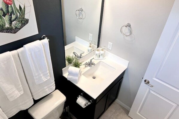Une salle de bain avec un lavabo blanc, un meuble noir et un grand miroir. Deux serviettes blanches sont suspendues à un porte-serviettes.