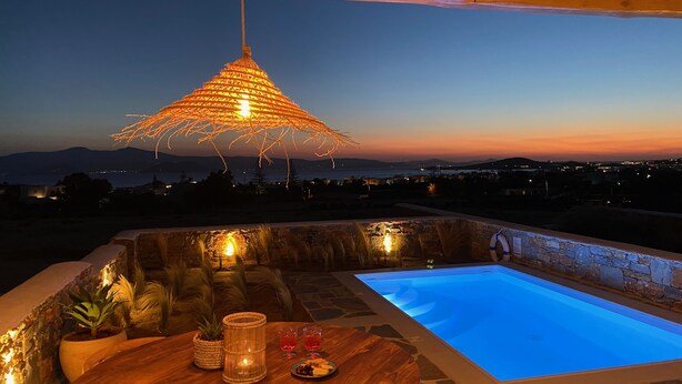 A cozy outdoor seating area with a pool, stone walls, and a hanging light fixture. - Beachhouse Omega Naxos - luxury holiday house - private pool & stunning sea view (Naxos)