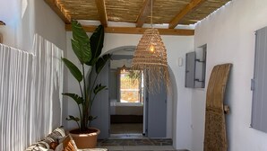 A cozy interior with a wooden ceiling, a woven hanging light fixture, a stone floor, and a view through an open doorway. - Beachhouse Omega Naxos - luxury holiday house - private pool & stunning sea view (Naxos)