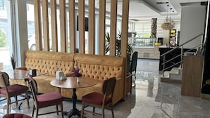 Un moderno vestíbulo de hotel con un área de estar que incluye un sofá capitonado y sillas rojas, una mesa redonda de madera y un separador decorativo de madera.