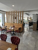 Un moderno vestíbulo de hotel con un área de estar que incluye un sofá capitonado y sillas rojas, una mesa redonda de madera y un separador decorativo de madera.