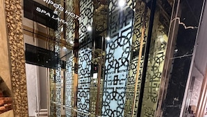 Un ascensor con intrincados diseños geométricos en paredes y suelo, que conduce a la entrada de un hotel.