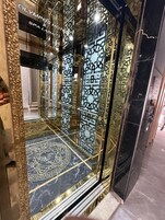 Un ascensor con intrincados diseños geométricos en paredes y suelo, que conduce a la entrada de un hotel.