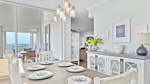 Un comedor moderno con una mesa larga, sillas blancas y vista al océano.
