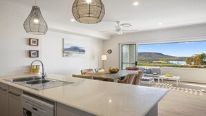 Une cuisine moderne dotée d’un grand îlot central, d’un coin repas avec des meubles en osier, et offrant une vue sur un paysage montagneux grâce à de grandes fenêtres.
