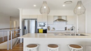 Une cuisine moderne dotée d’un îlot central, d’appareils électroménagers en acier inoxydable et d’un luminaire suspendu.
