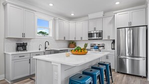 A modern kitchen with white cabinetry, stainless steel appliances, and a central island with stools. - Super Cute House on the Cape - Walk to Beach - Dog Friendly! (Port St Joe)