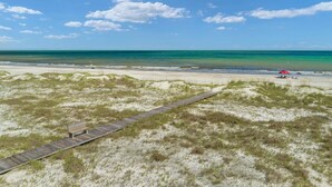 A beach with a wooden boardwalk leading to a red umbrella and beach chairs. - Super Cute House on the Cape - Walk to Beach - Dog Friendly! (Port St Joe)