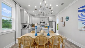 A modern kitchen with white cabinets, a central island, and a dining area with a wooden table and wicker chairs. - Super Cute House on the Cape - Walk to Beach - Dog Friendly! (Port St Joe)