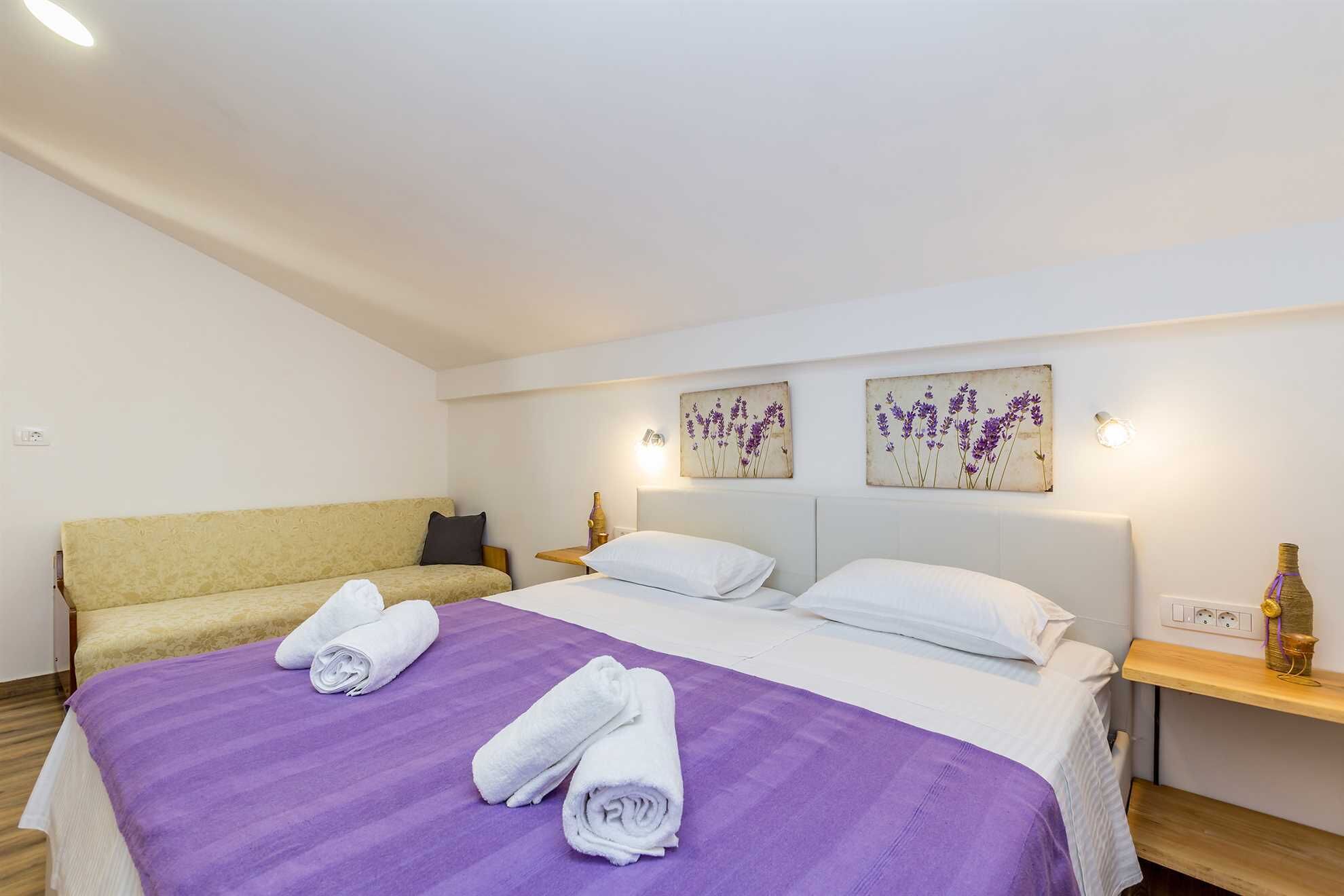 A hotel room with a bed, a sofa, and two wall-mounted light fixtures.
