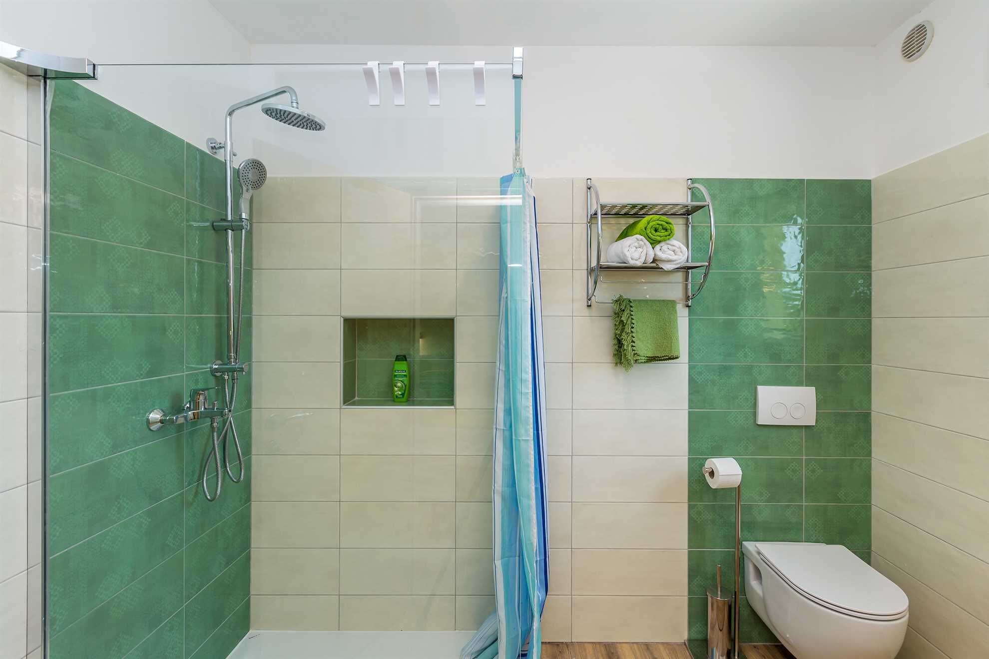 Een badkamer met een douche, toilet en een plank met handdoeken en toiletartikelen.