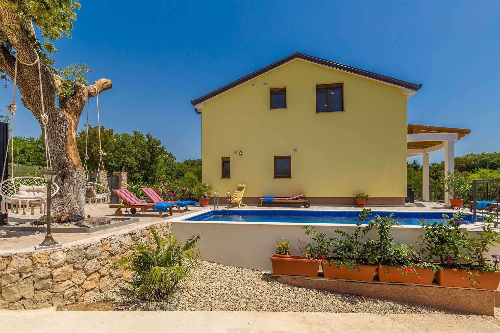 Uma casa amarela de dois andares com piscina, área de estar ao ar livre e pérgula.
