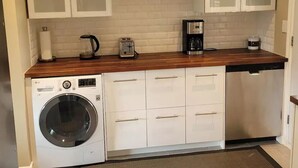 Une cuisine compacte avec des meubles blancs, un lave-linge, une machine à café et un grille-pain.