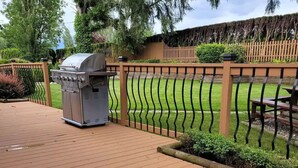 Une terrasse en bois avec un barbecue et une clôture en métal.