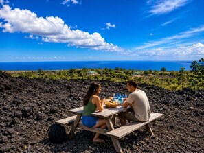 A couple dining at a wooden picnic table with a view of the ocean.