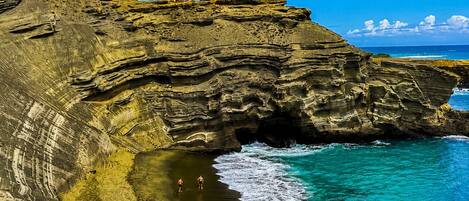 Un paisaje costero con formaciones rocosas escalonadas, una playa y aguas azules cristalinas.
