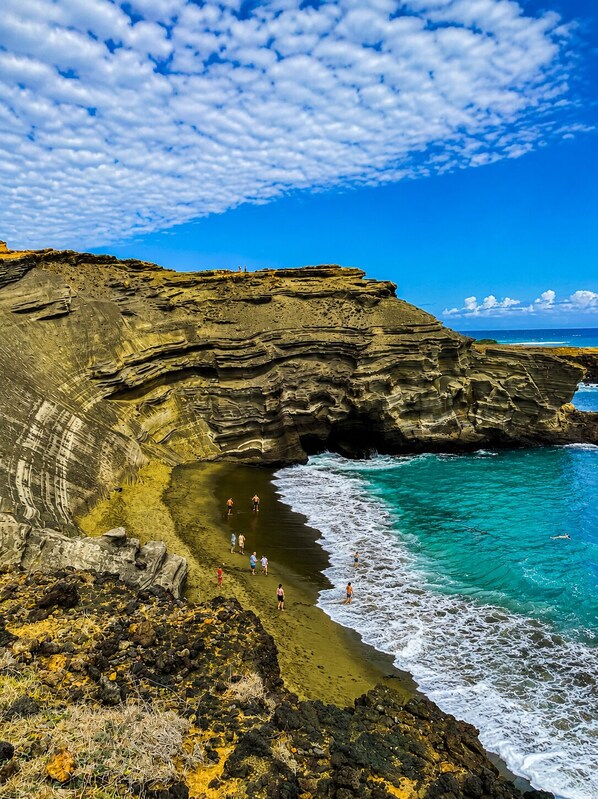 A coastal landscape with layered rock formations, a beach, and clear blue waters.