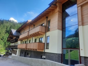 Un hotel de varios pisos con balcones de madera, ventanas grandes y vistas a una montaña boscosa.