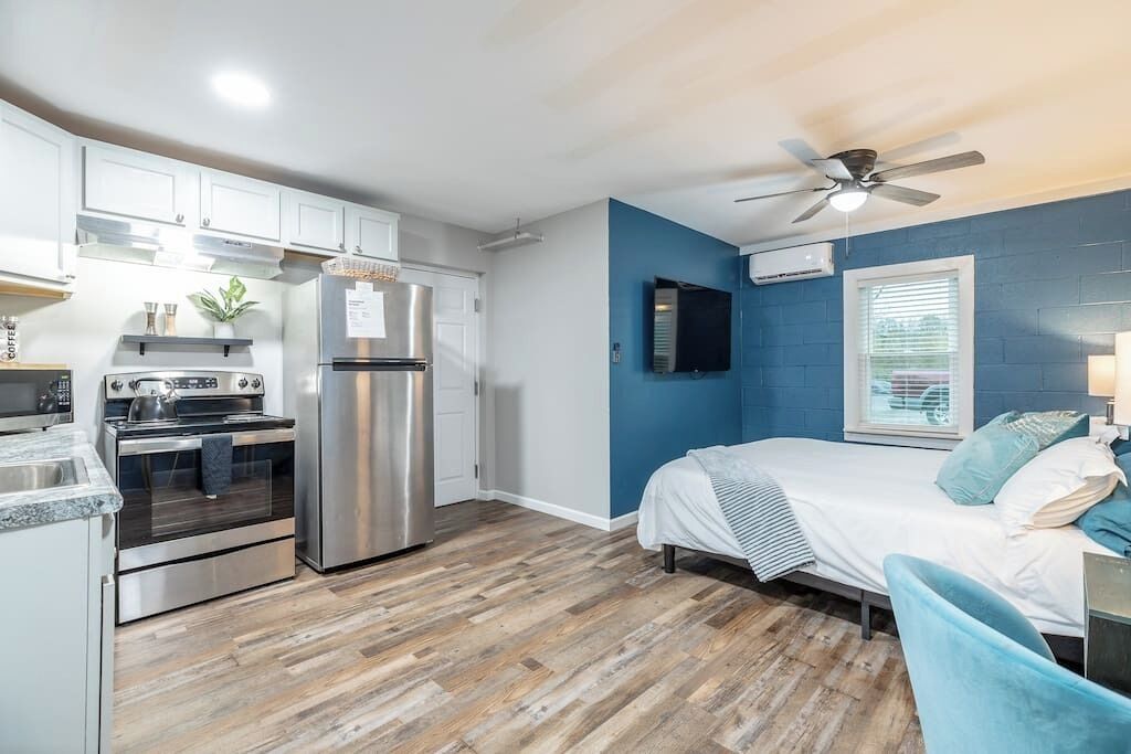 A compact kitchen with modern appliances, a dining area, and a bedroom with a bed and a ceiling fan.
