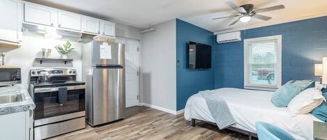 A compact kitchen with modern appliances, a dining area, and a bedroom with a bed and a ceiling fan.