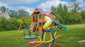 A wooden playhouse with a slide and climbing wall, surrounded by a grassy yard. - Suite 118 - Harmony at Rock Spring Resort (Rock Spring)