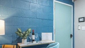 A room with a blue brick wall, a wooden floor, a light blue door, a desk with a chair, a plant, a wine bottle, and a framed certificate. - Suite 118 - Harmony at Rock Spring Resort (Rock Spring)