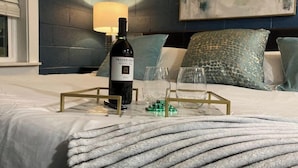 A neatly made bed with a bottle of wine, glasses, and a tray on a marble surface. - Suite 118 - Harmony at Rock Spring Resort (Rock Spring)
