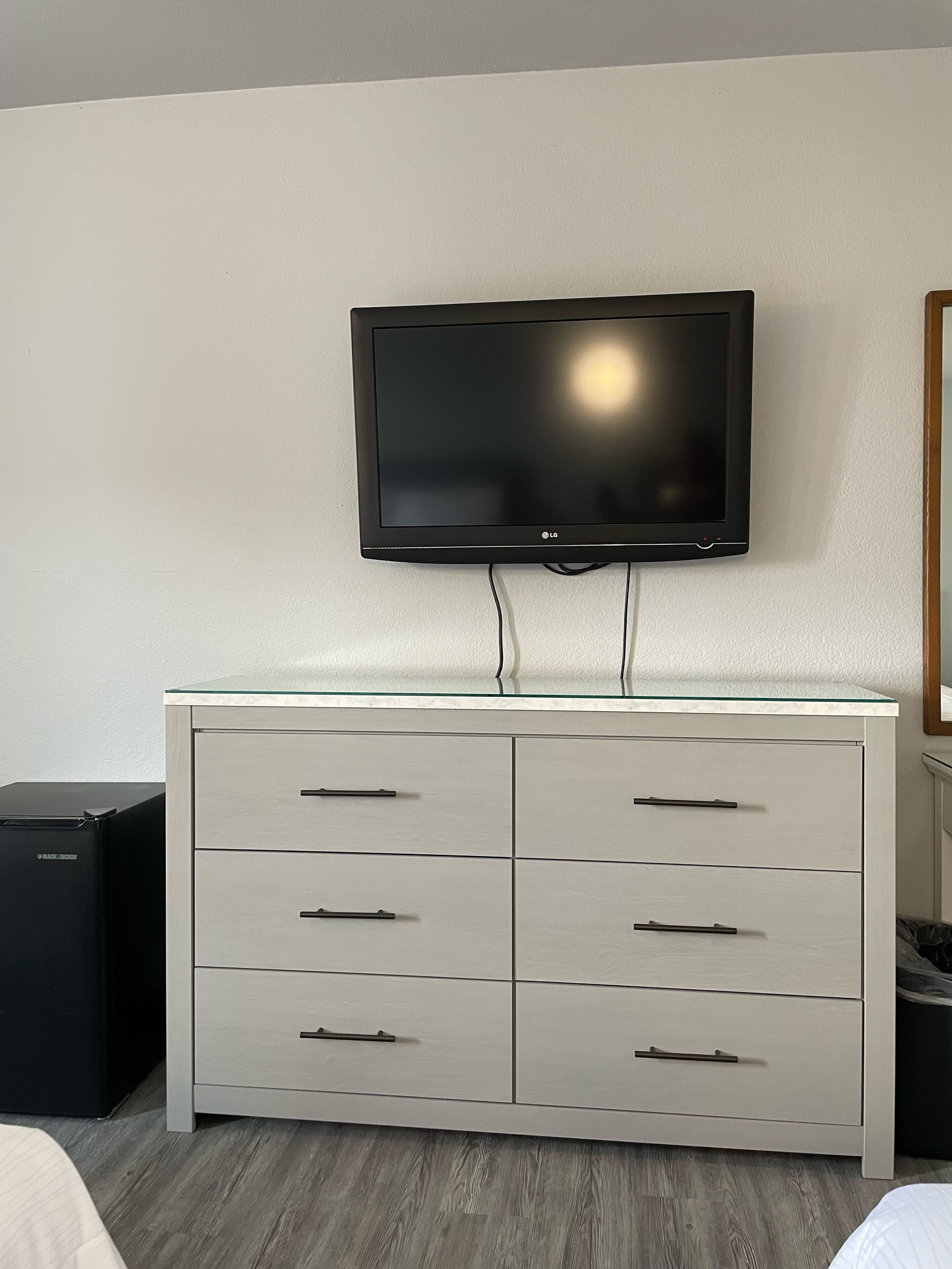 Une chambre d’hôtel moderne dotée d’un téléviseur à écran plat fixé au mur, au-dessus d’une commode blanche à plusieurs tiroirs.