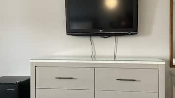 Ett modernt hotellrum med en platt-TV som är monterad på väggen ovanför en vit byrå med flera lådor.