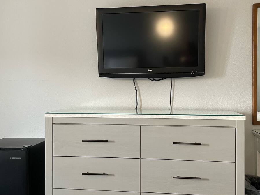 Ett modernt hotellrum med en platt-TV som är monterad på väggen ovanför en vit byrå med flera lådor.