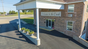 A building with a sign reading "Welcome to the Creek" and a covered entrance with potted plants. - Schmidt's Creek Hotel (Osage Beach)