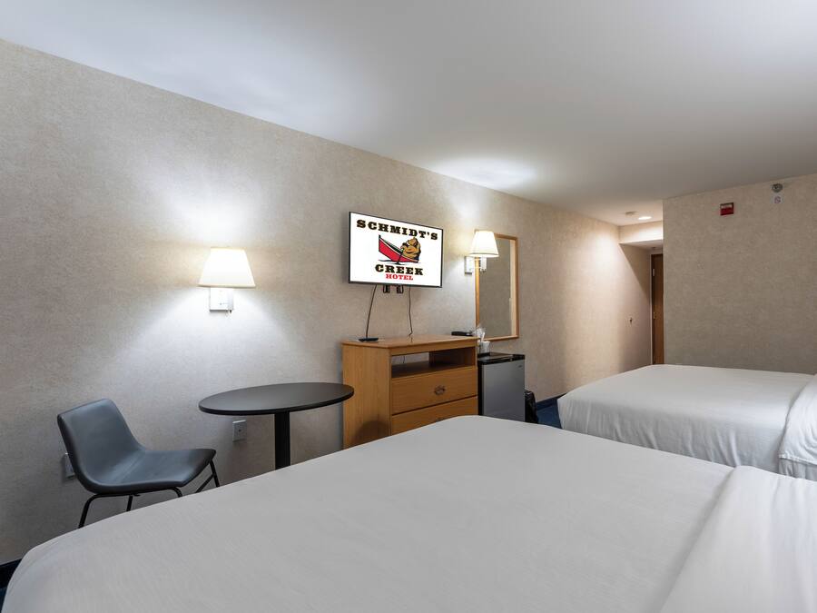 A hotel room with two beds, a desk, a chair, and a small table.